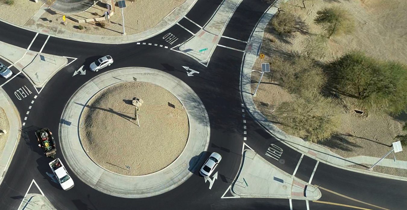 An aerial view of a crossroads roundabout in the desert with several cars going around in it